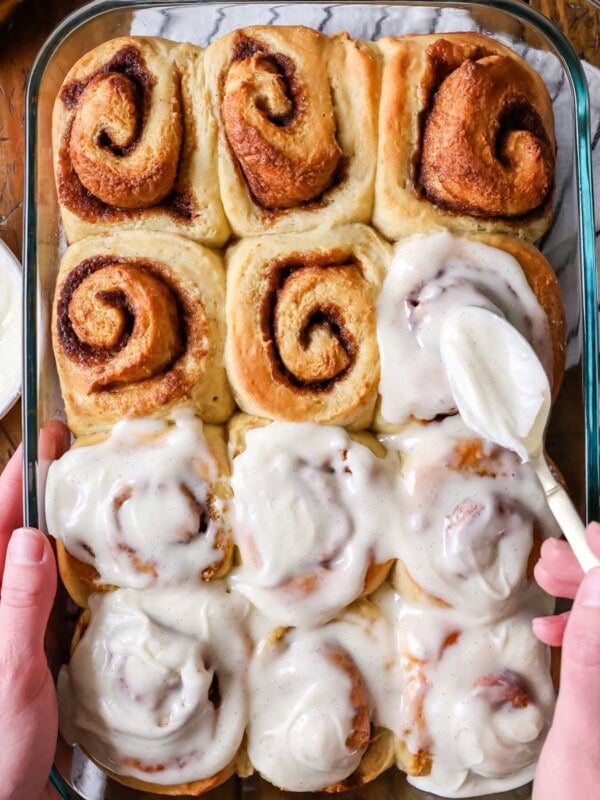 Overhead view of banana bread cinnamon rolls being frosted with cream cheese icing.