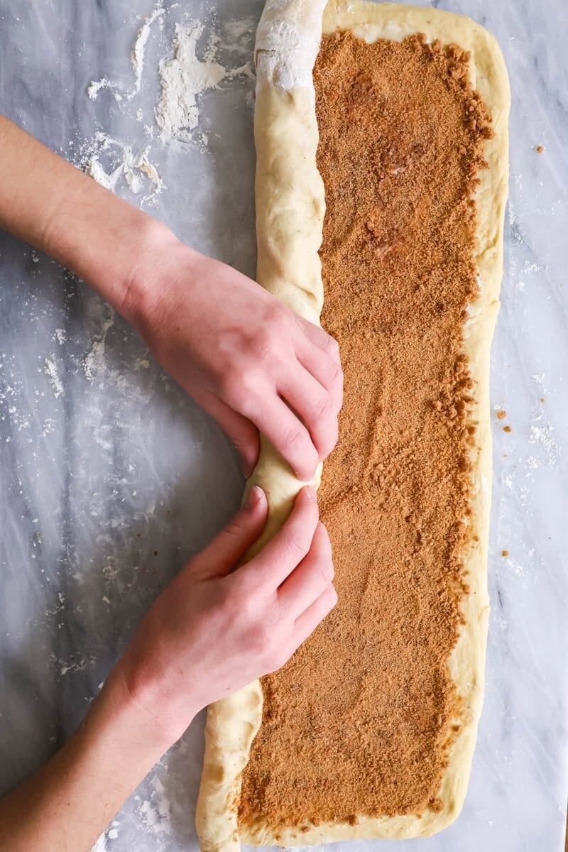 Hands rolling banana cinnamon roll dough into a log.