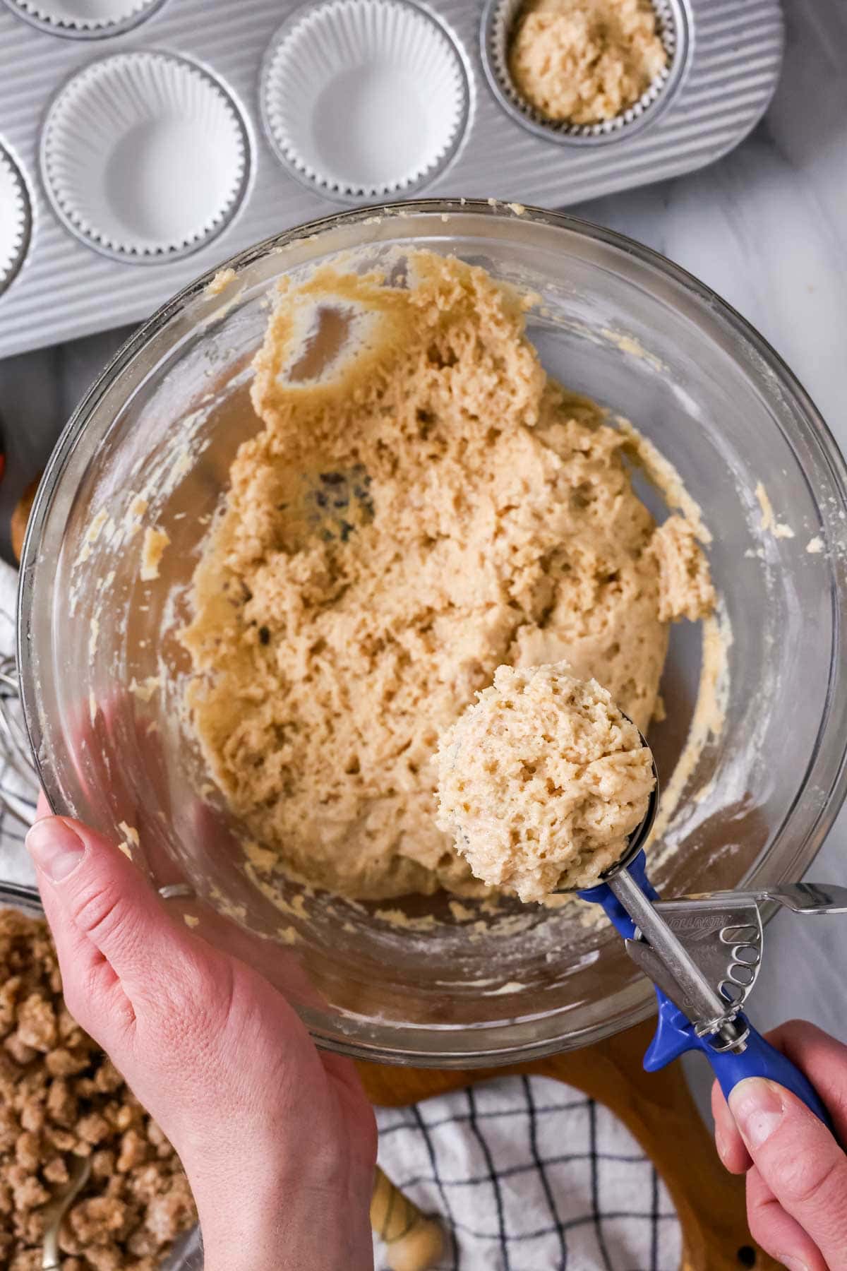 Muffin batter being scooped out of a bowl with an ice cream scoop.