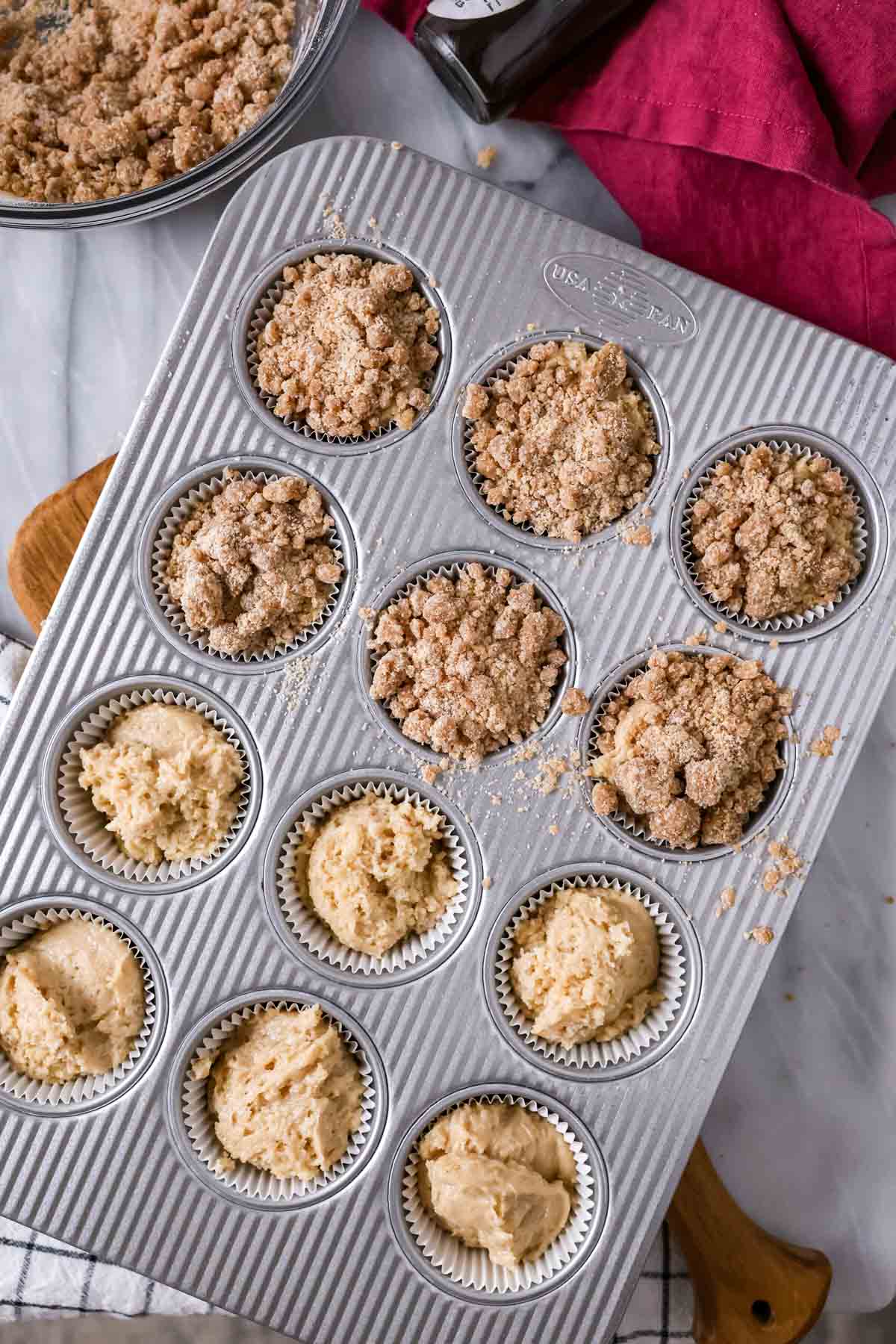 Streusel being sprinkled over muffin batter in a pan.