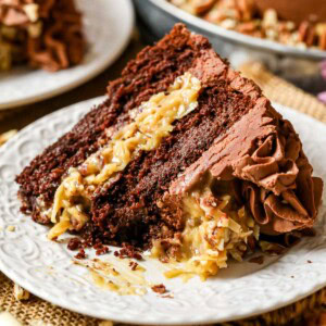 Slice of German chocolate cake on a plate with one bite missing.