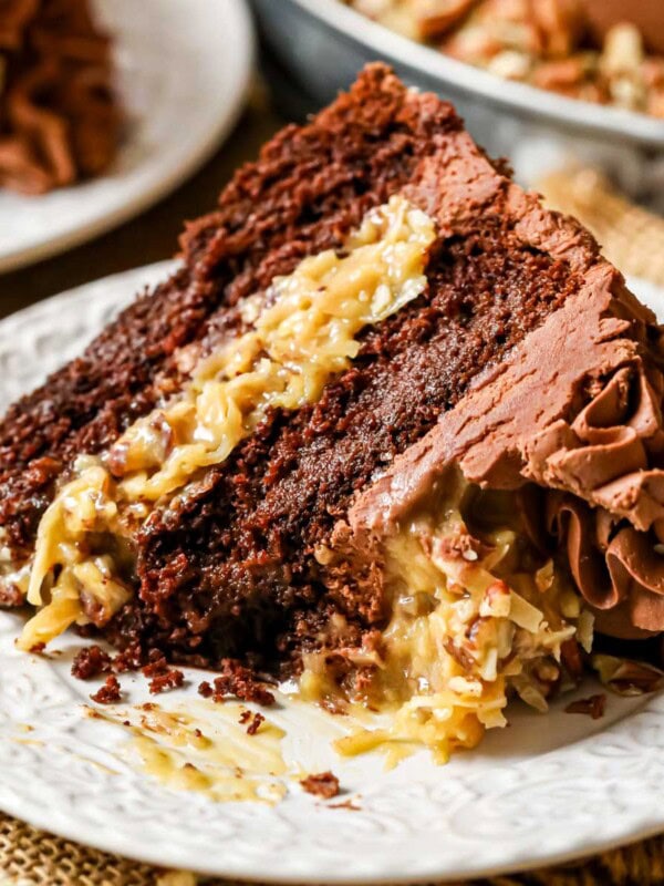 Slice of German chocolate cake on a plate with one bite missing.