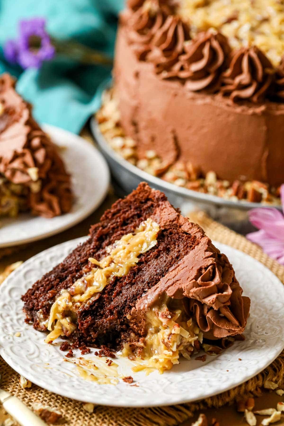 Slice of German chocolate cake on a plate with one bite missing.