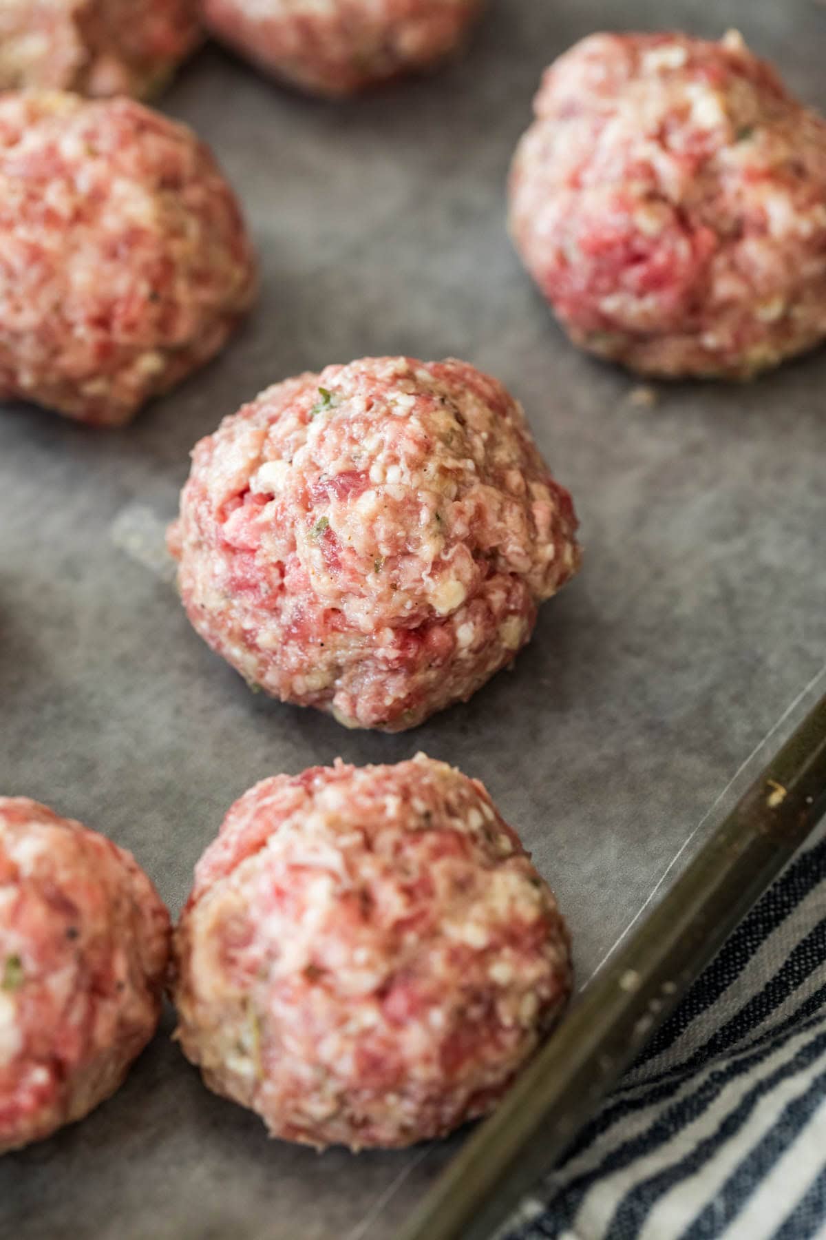 Raw meatballs on a baking sheet after being rolled by hand.
