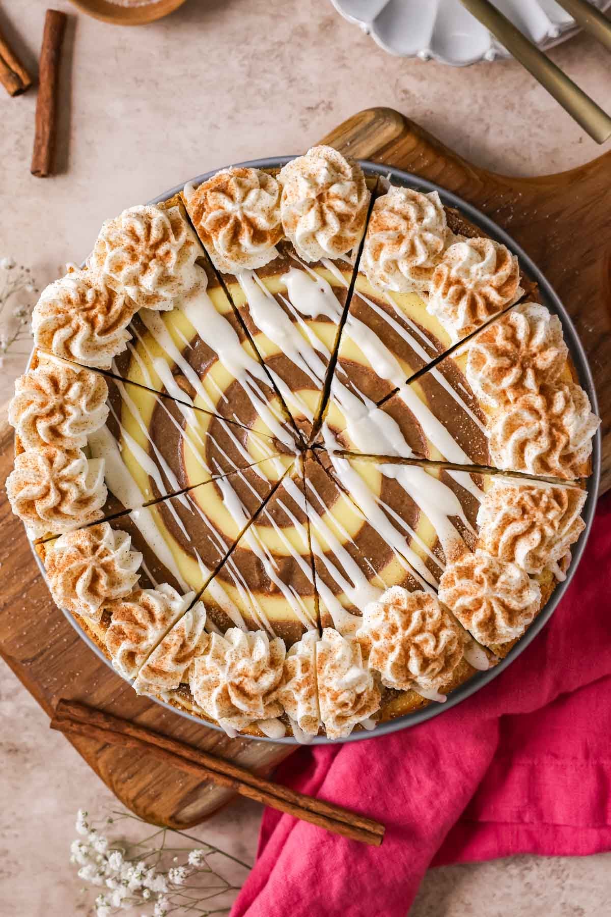 Overhead view of a cinnamon roll cheesecake that has been cut into 9 slices.
