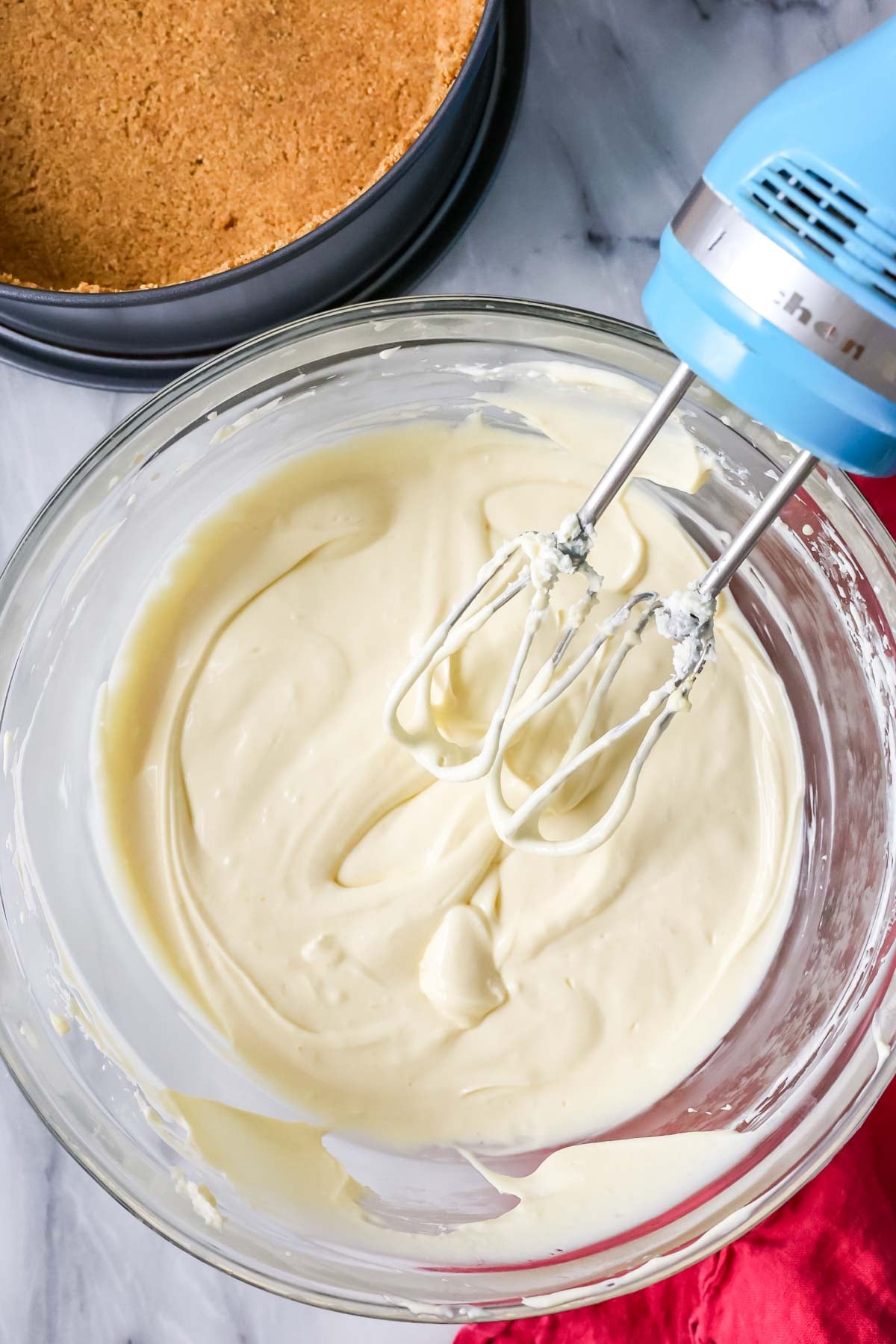 Overhead view of a bowl of cheesecake batter that's been mixed with a hand mixer.