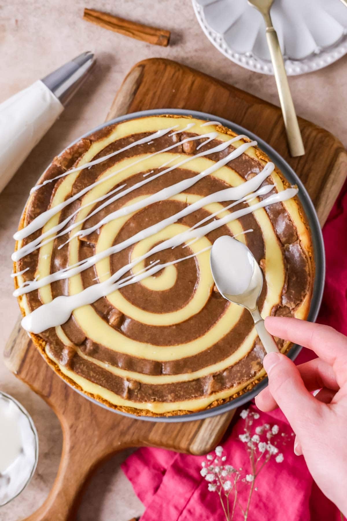 Drizzling vanilla glaze of a cinnamon roll cheesecake.