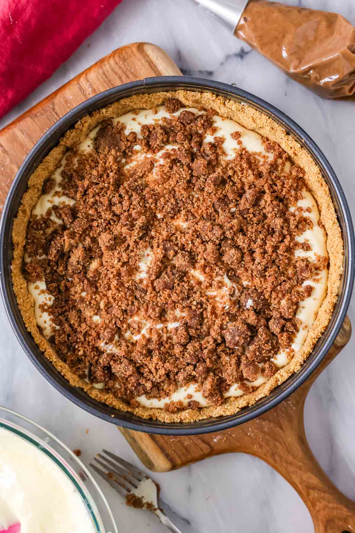 Overhead view of a layer of brown sugar and cinnamon crumbles over cheesecake batter in a pan.
