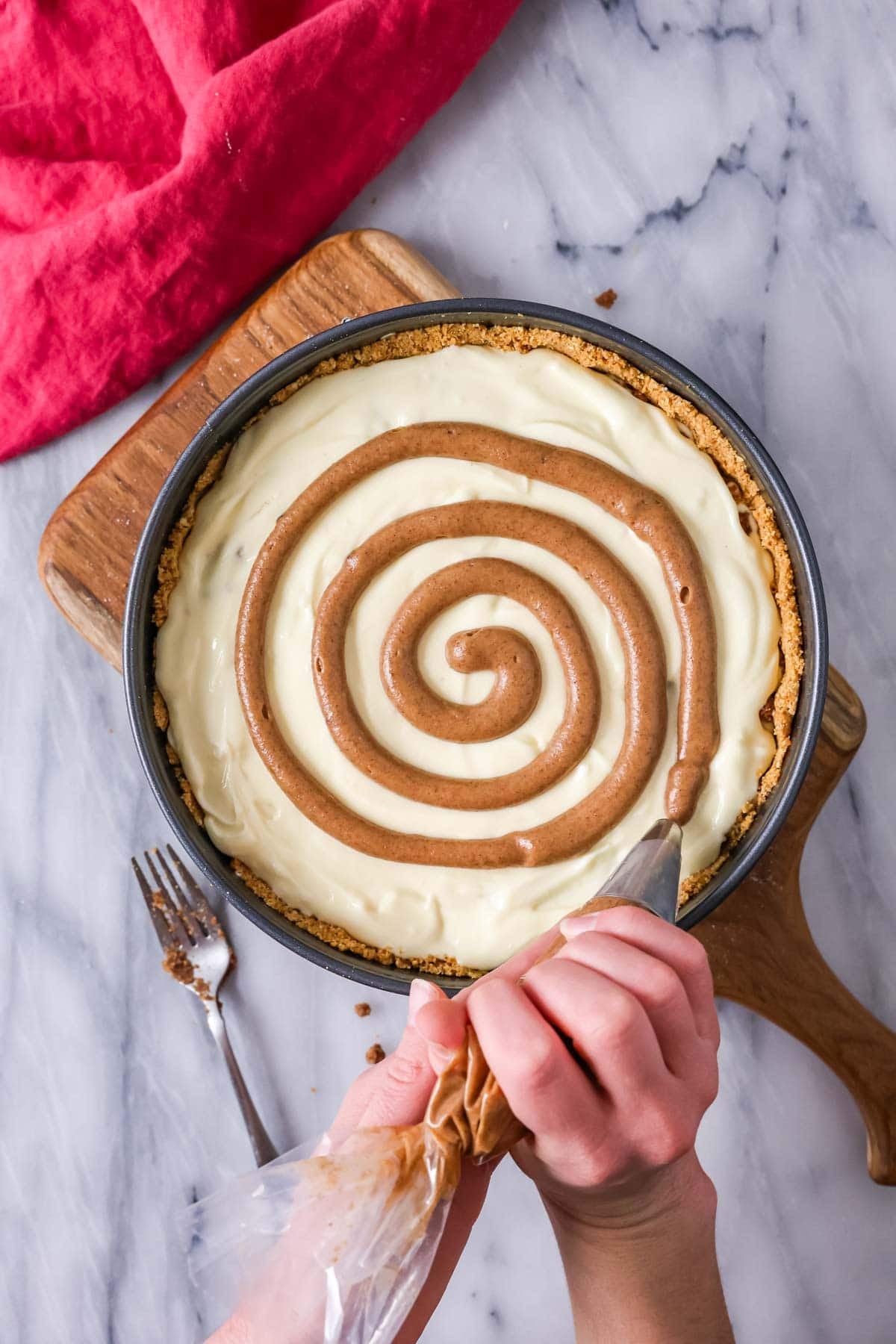 Piping a brown sugar cinnamon swirl over cheesecake batter in a pan.