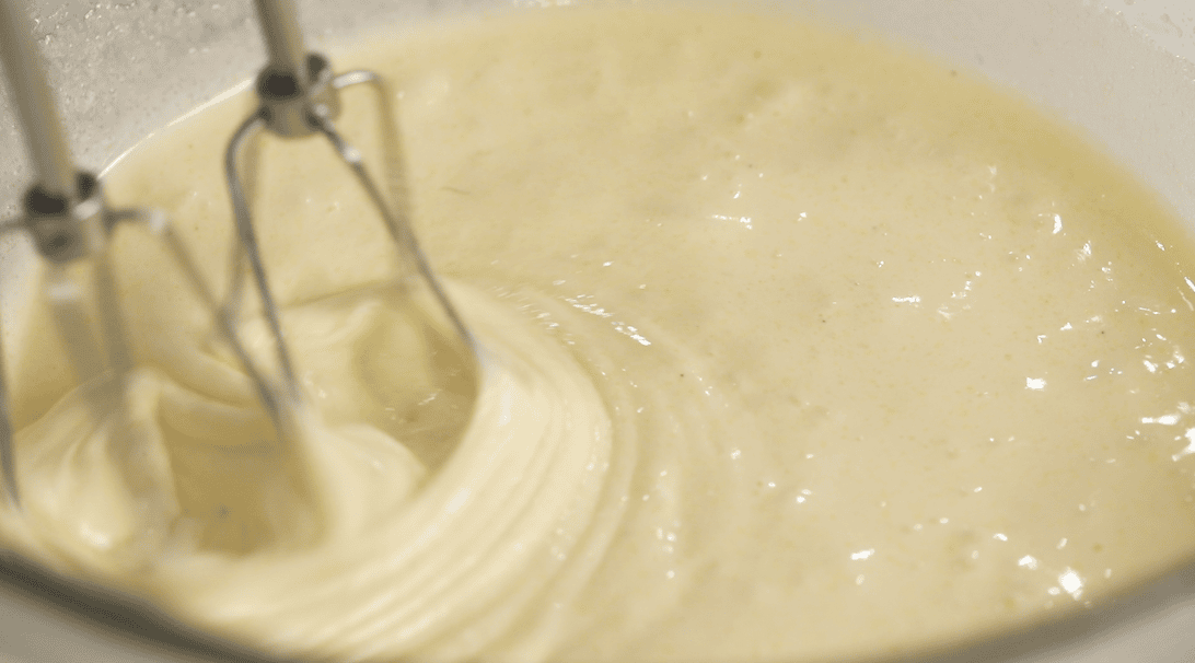 Close-up of eggs, sugar, and vanilla being mixed with an electric mixer.