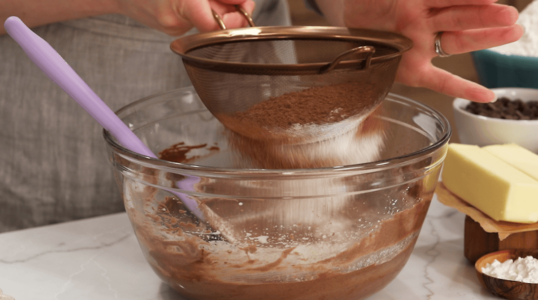 Sifting flour and cocoa powder over a batter.
