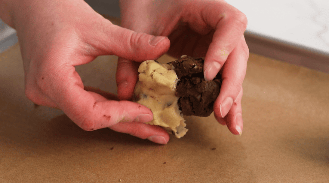 Hands pressing chocolate chip cookie dough and brownie cookie dough together.