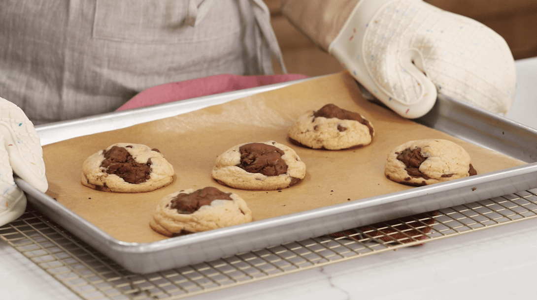 Baking sheet of brookie cookies being set on a cooling rack after baking.