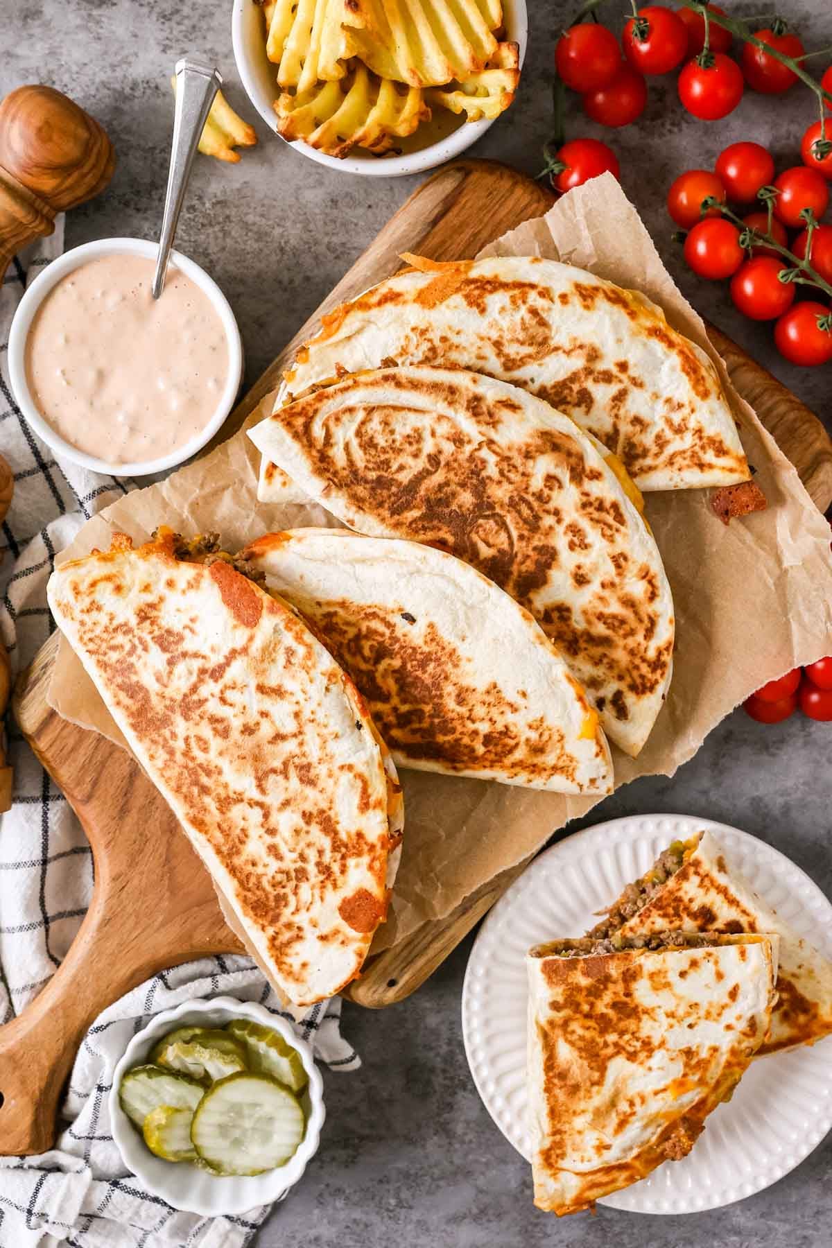 Overhead view of quesadillas on a serving platter with pickles, waffle fries, and burger sauce around them.