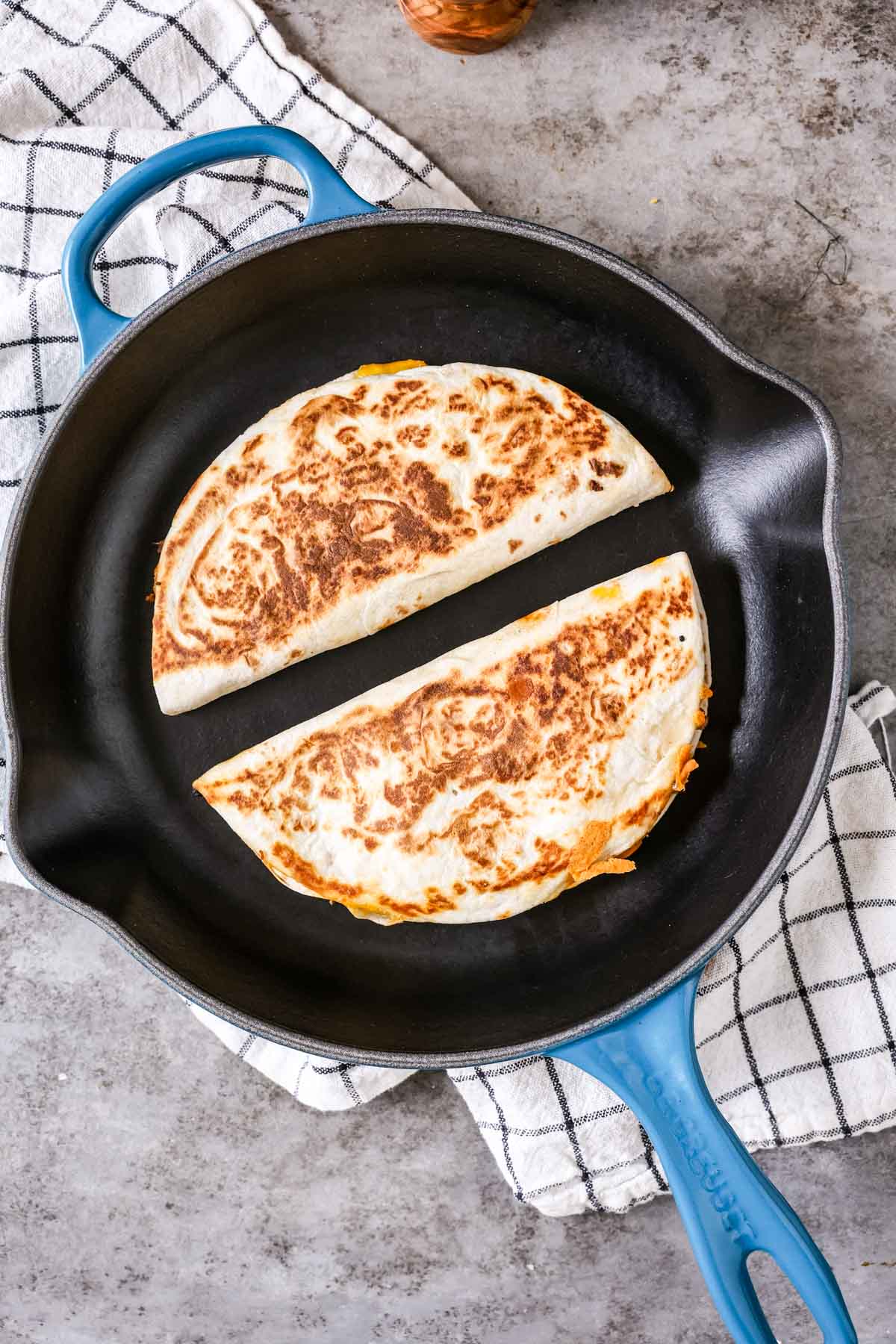 Overhead view of two golden brown quesadillas cooking in a pan.
