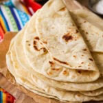 Pile of homemade flour tortillas with the top tortilla folded over.
