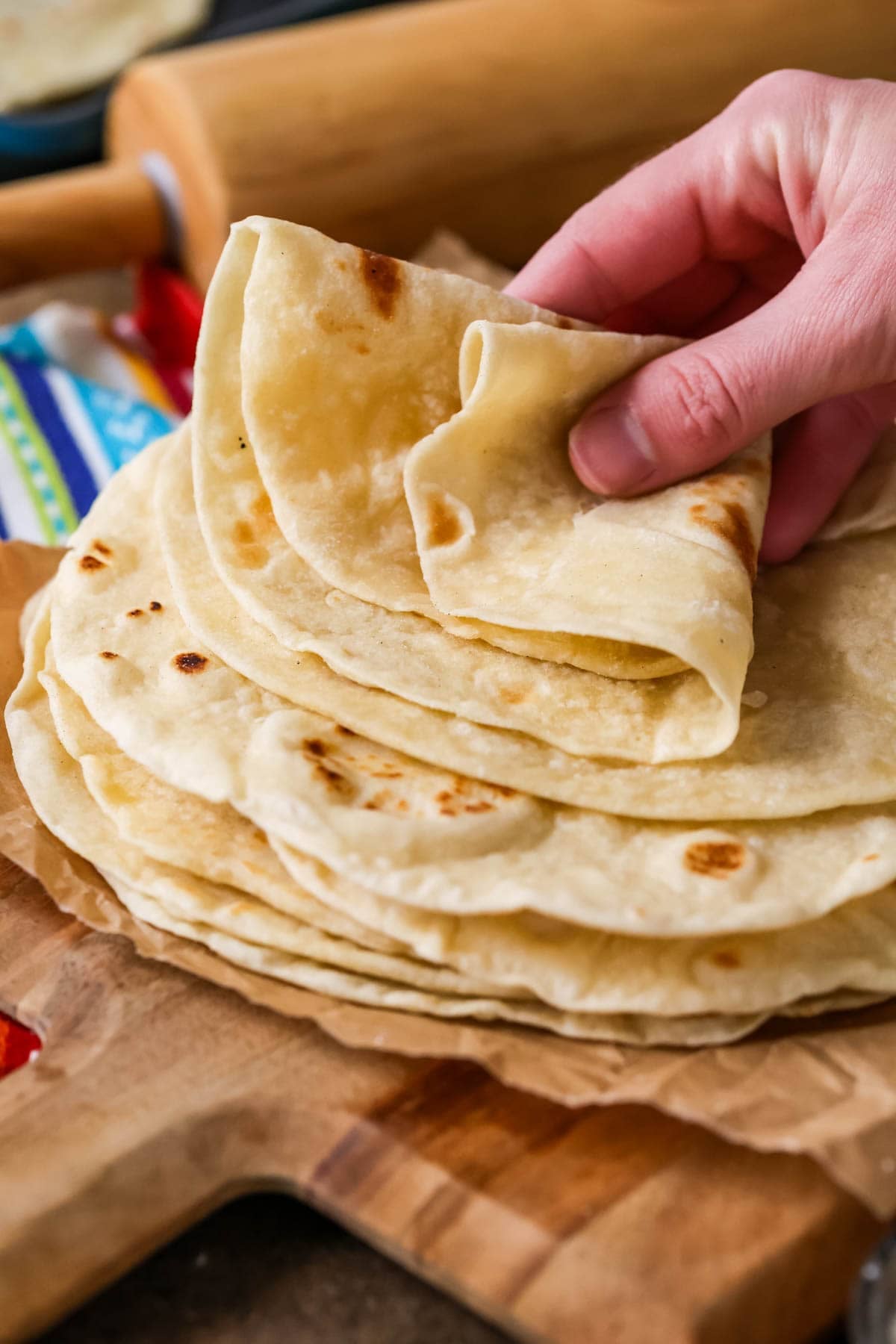 Hands grabbing a homemade tortilla off a stack.