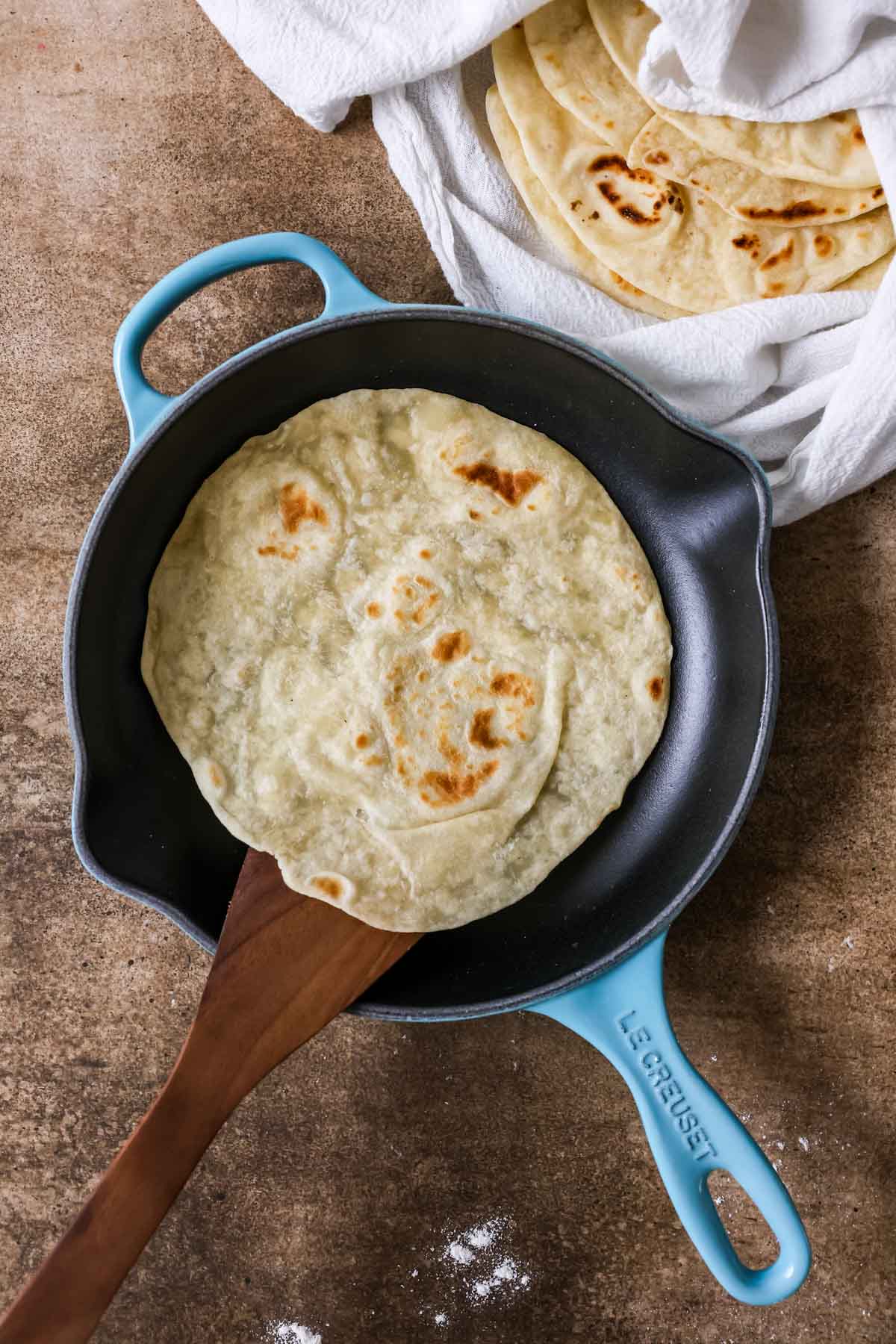 Overhead view of a tortilla cooking in a cast iron skillet.