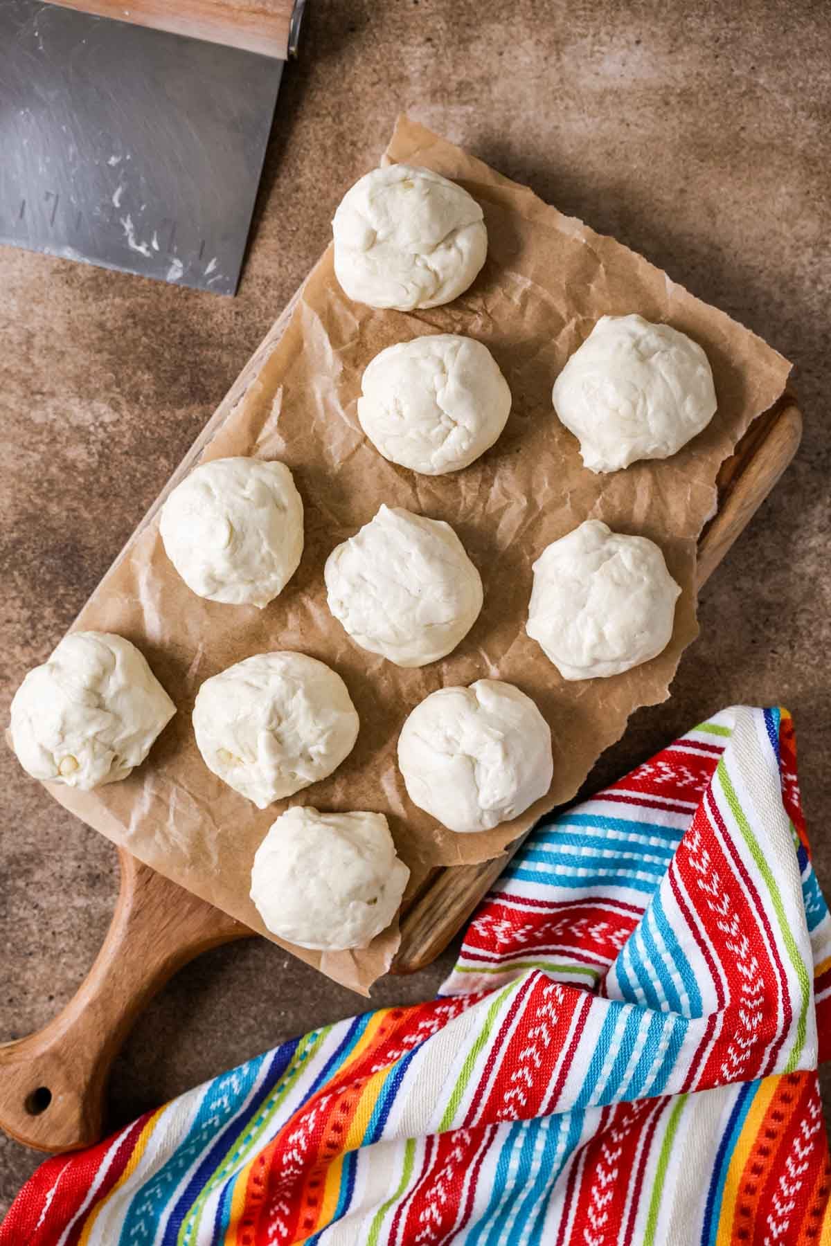 Overhead view of 10 dough balls on a wood cutting board.