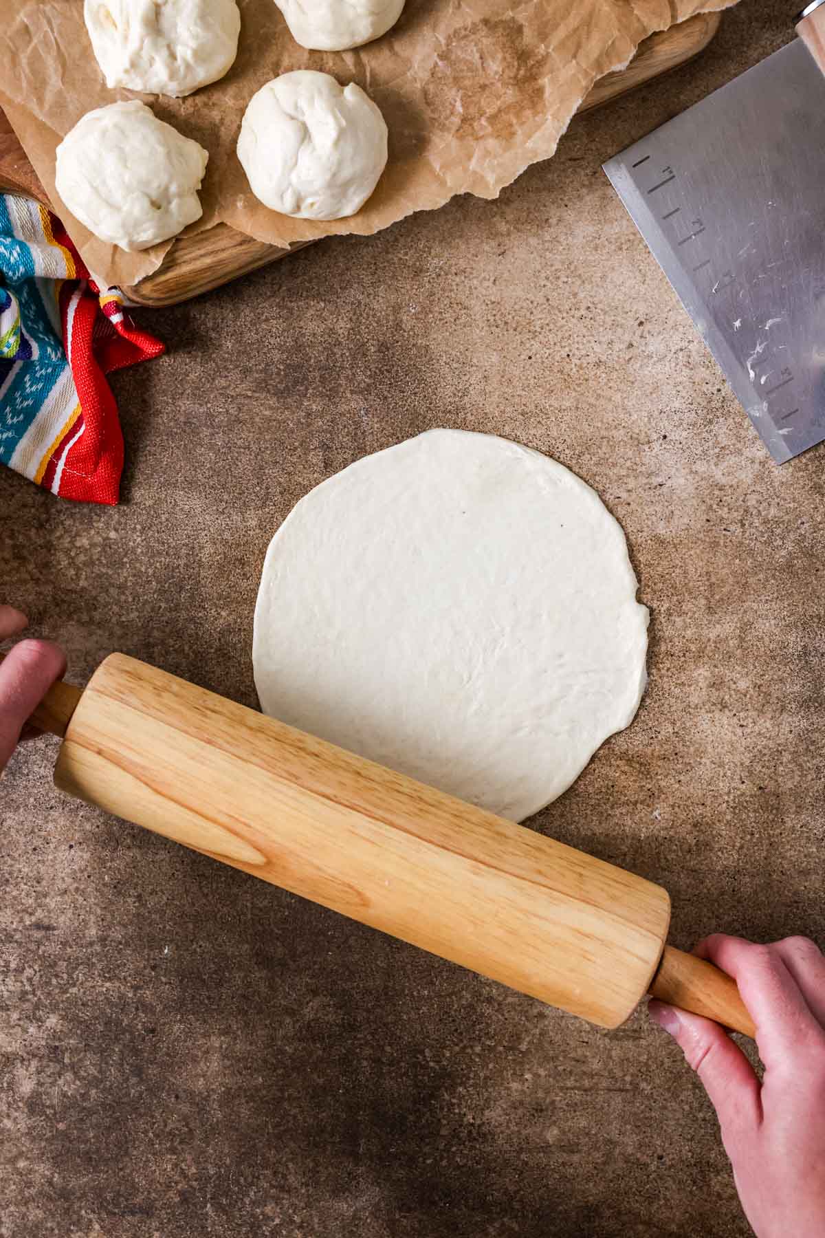 Overhead view of a rolling pin rolling out a flour tortilla.