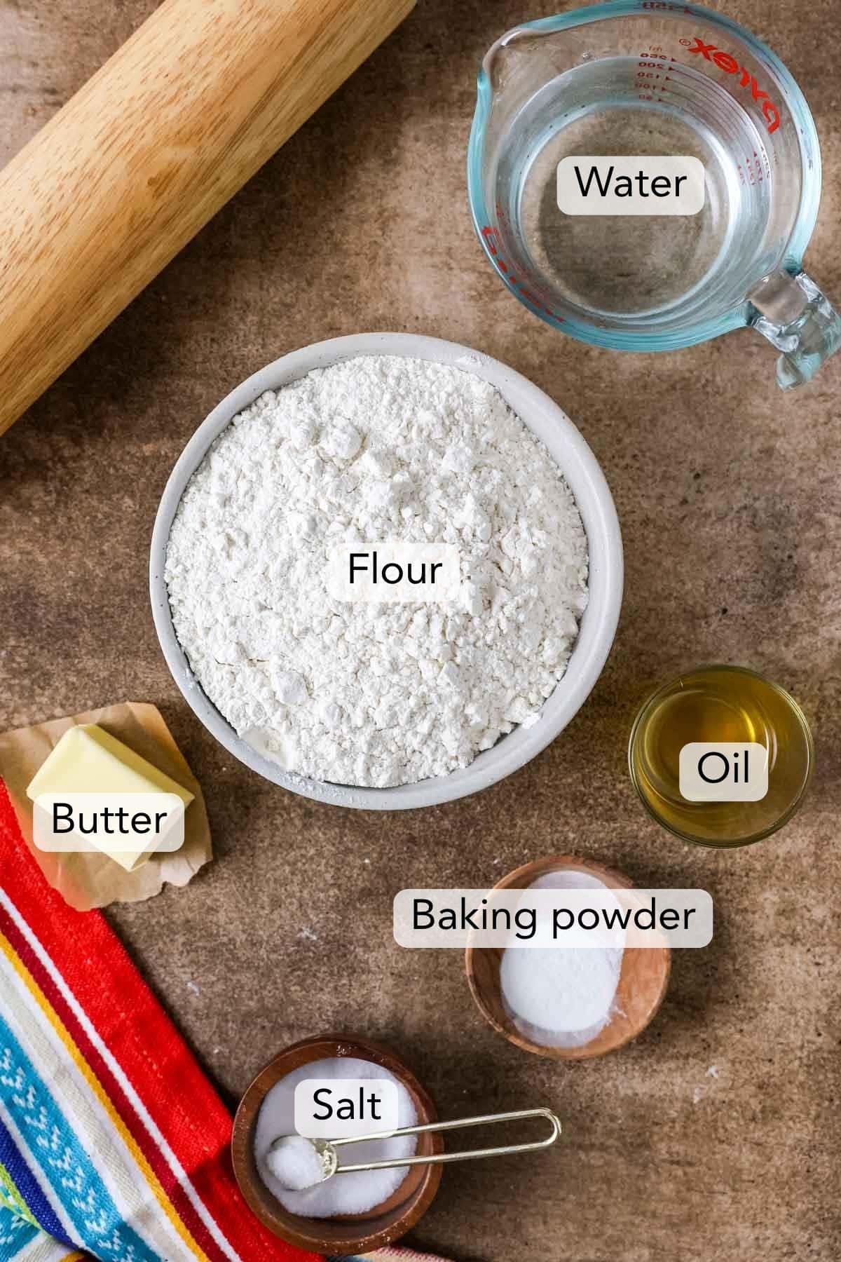 Overhead view of ingredients for flour tortillas including flour, butter, oil, salt, baking powder, and water.