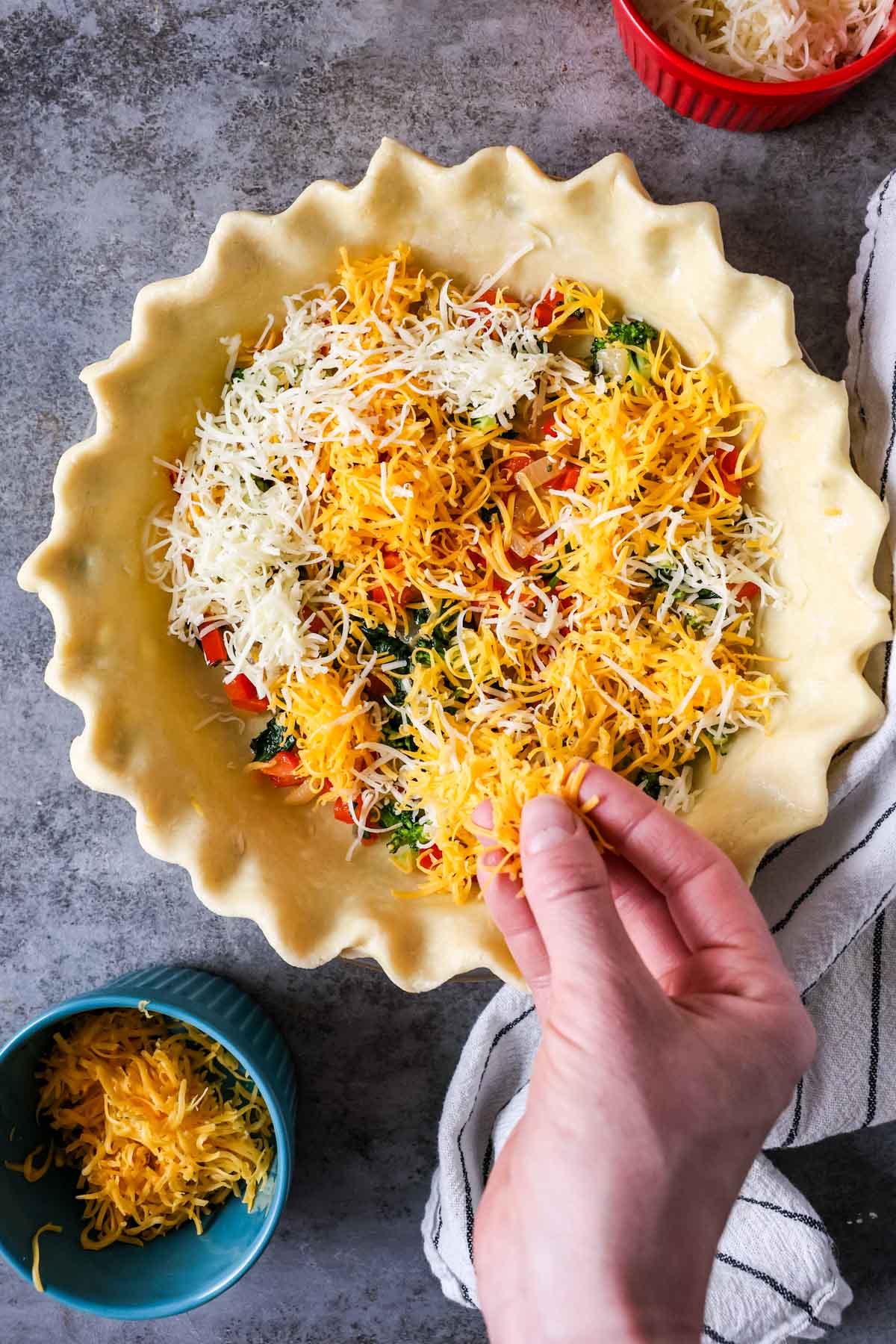 Sprinkling cheese over diced veggies in a pie crust.