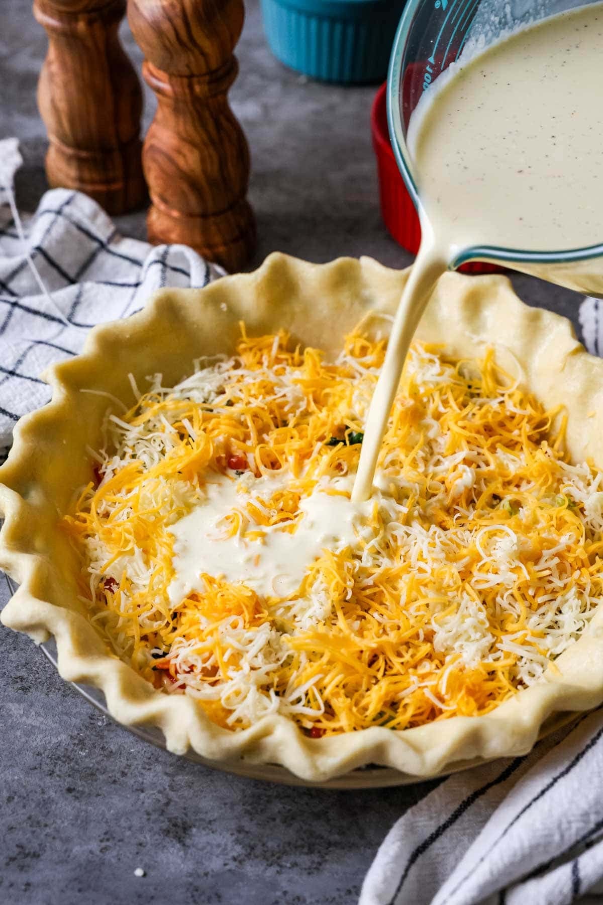 Pouring a custard mixture over cheese and veggies in a pie crust.