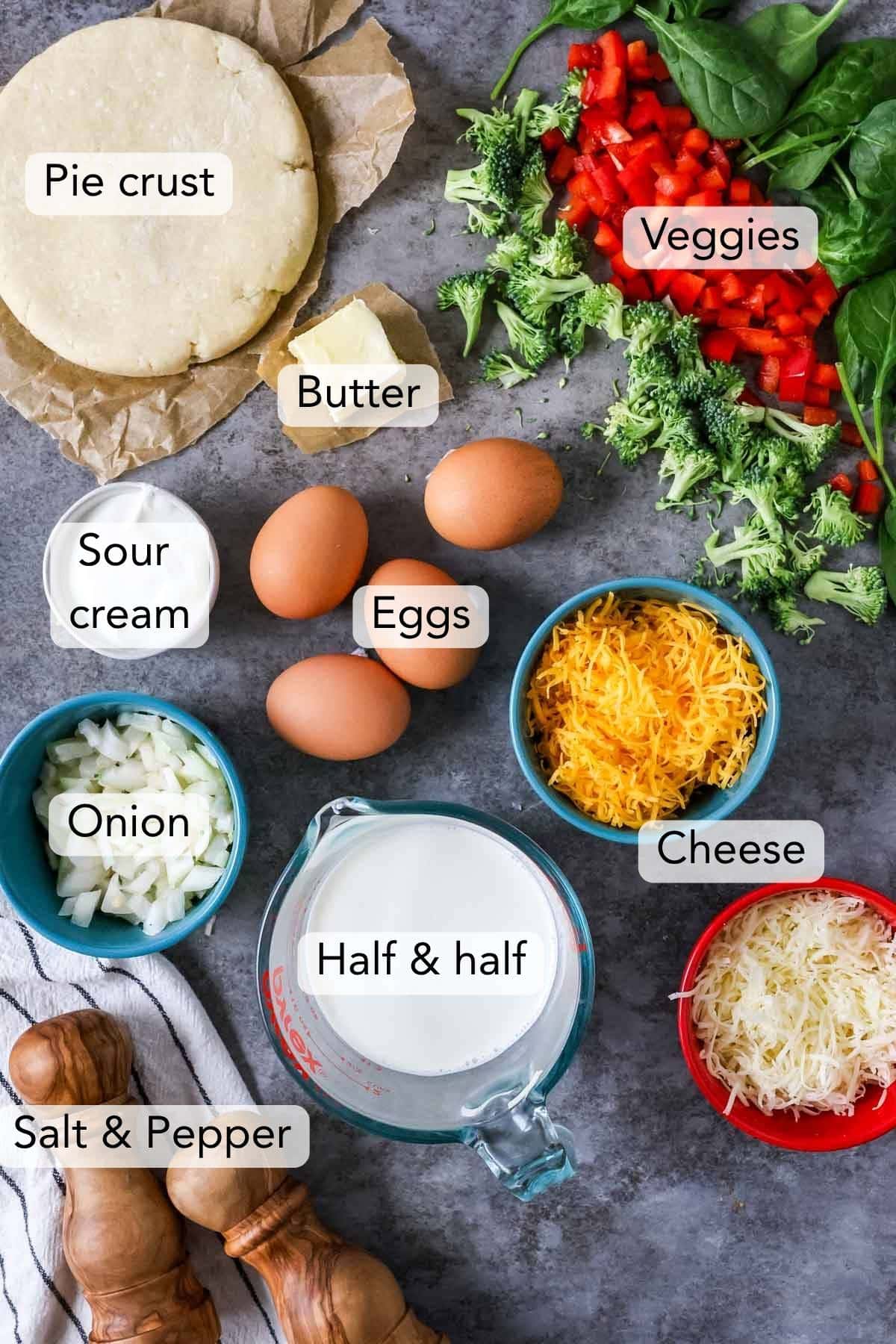 Overhead view of ingredients including eggs, diced veggies, cheese, pie crust, and more.
