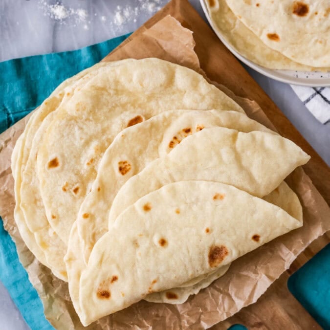 Pile of sourdough tortillas on a wood platter.