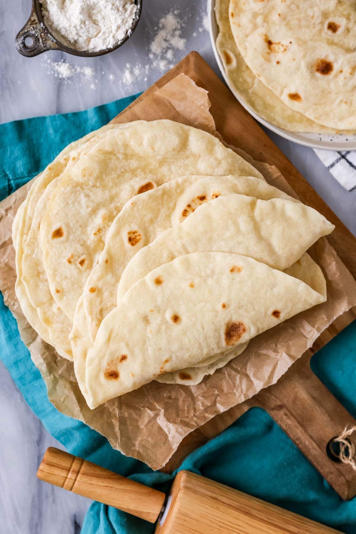 Pile of sourdough tortillas on a wood platter.
