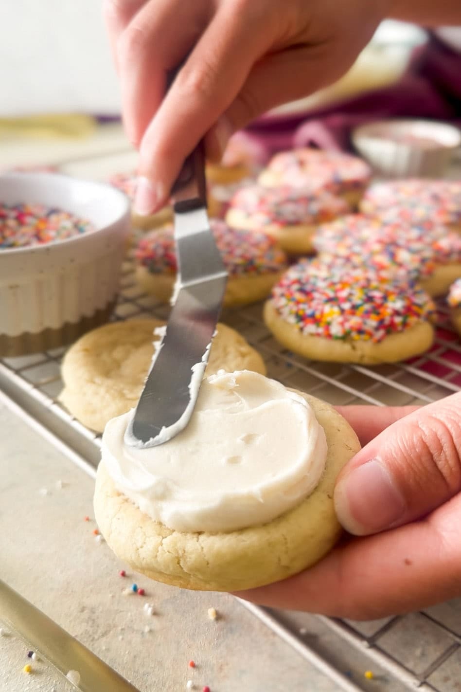 Using an offset spatula to smooth frosting over a thick cookie.