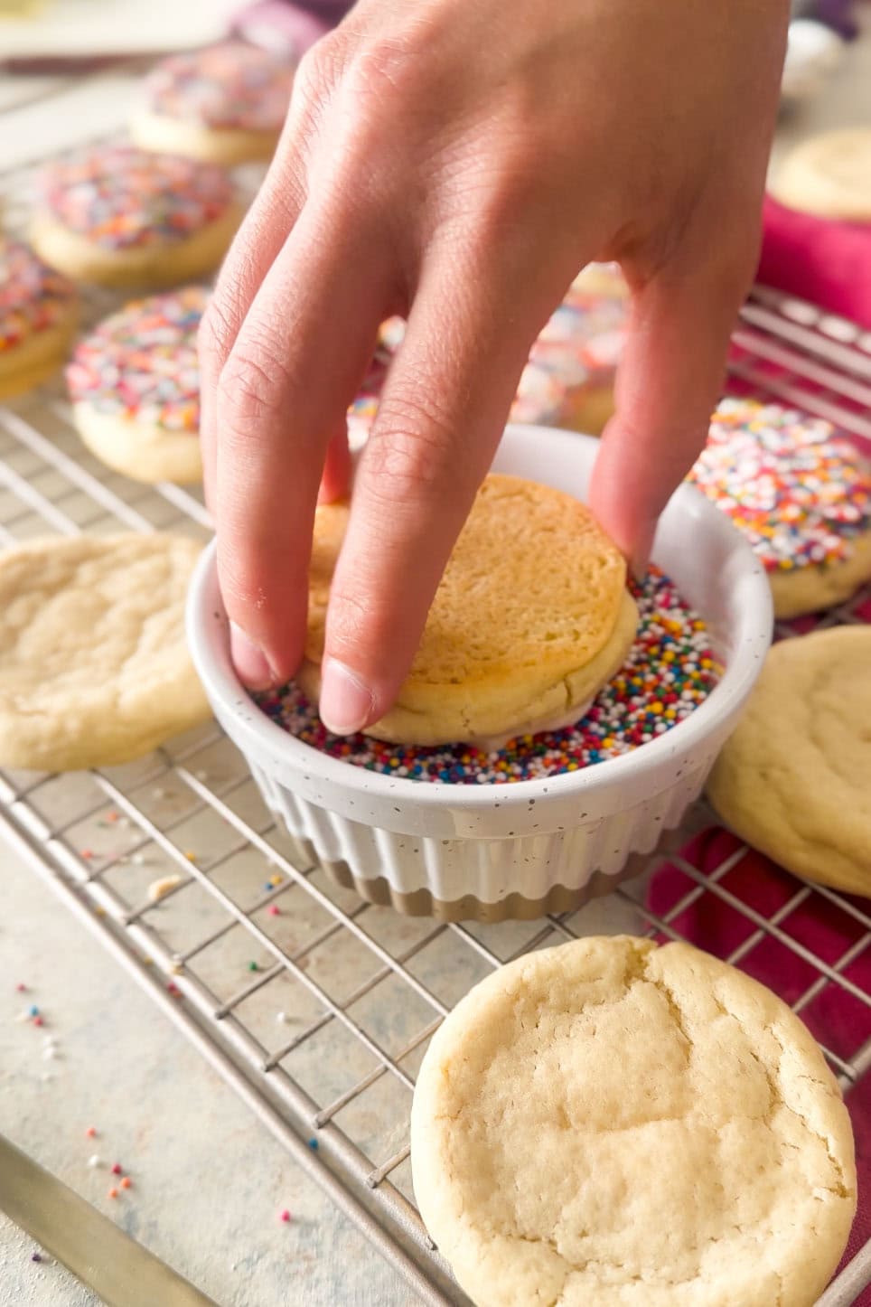 Dunking a frosted cookie in nonpareil sprinkles.