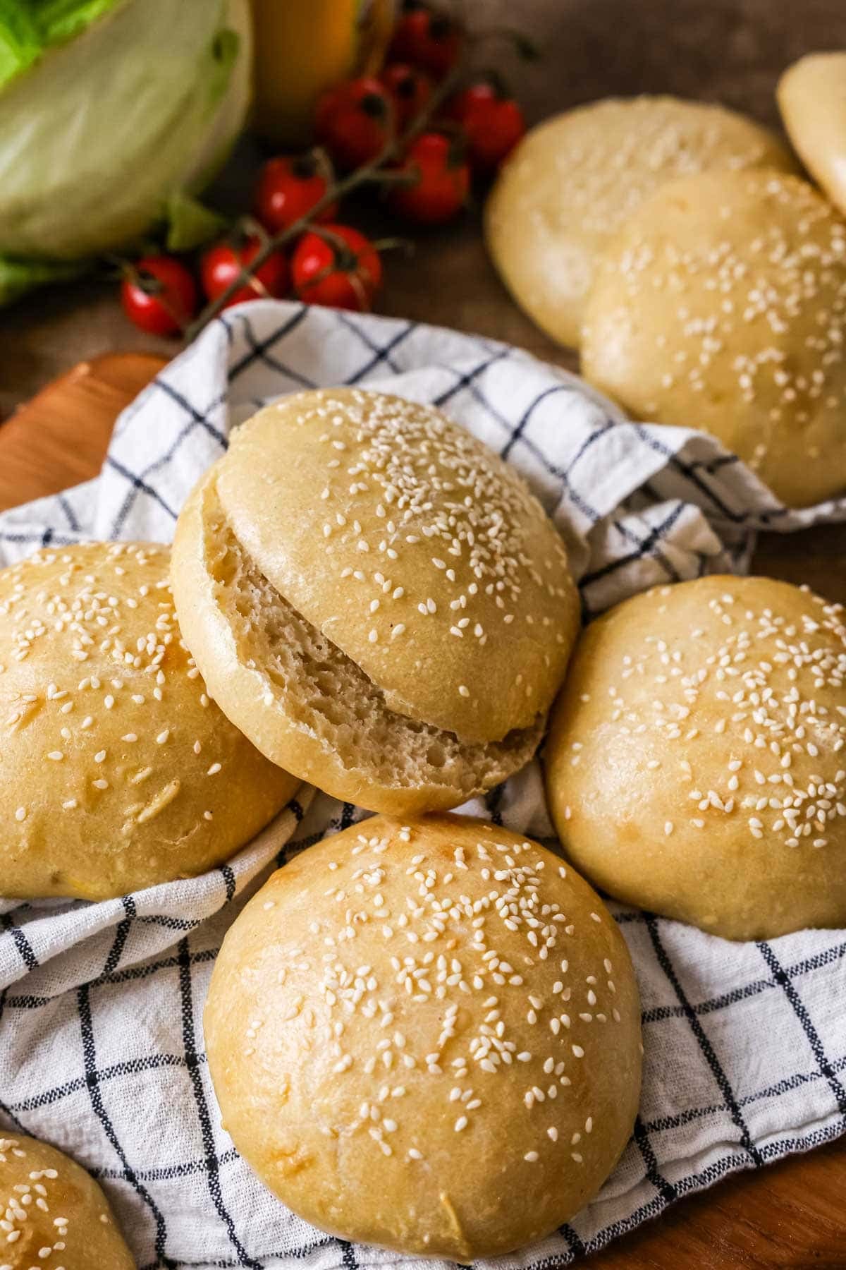 Overhead view of homemade sourdough hamburger buns topped with sesame seeds on a kitchen towel with one bun sliced in half.