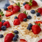 Close-up view of a berry icebox cake that's been cut into squares and topped with fresh berries and graham cracker crumbs.