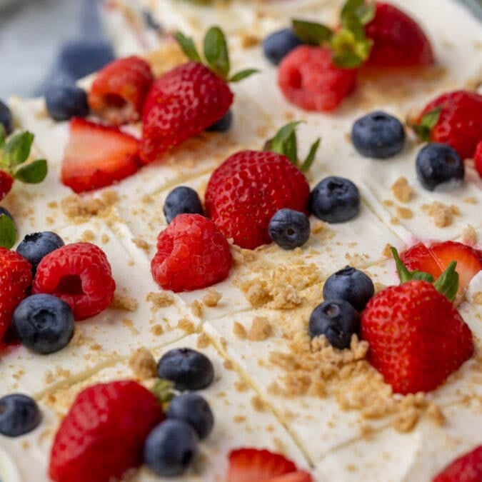 Close-up view of a berry icebox cake that's been cut into squares and topped with fresh berries and graham cracker crumbs.