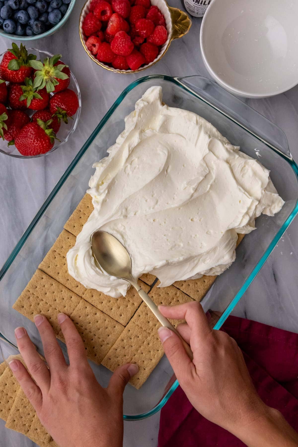 Spreading a whipped cream cheese mixture over graham crackers in a baking dish.