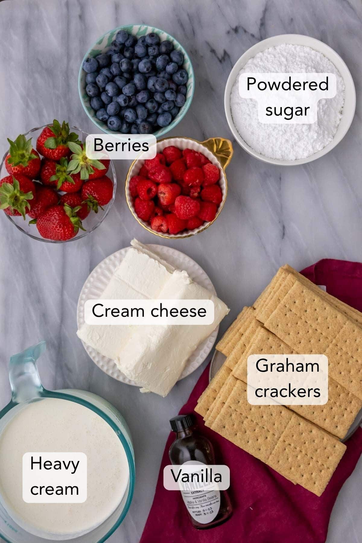 Overhead view of ingredients including berries, cream cheese, graham crackers, and more.