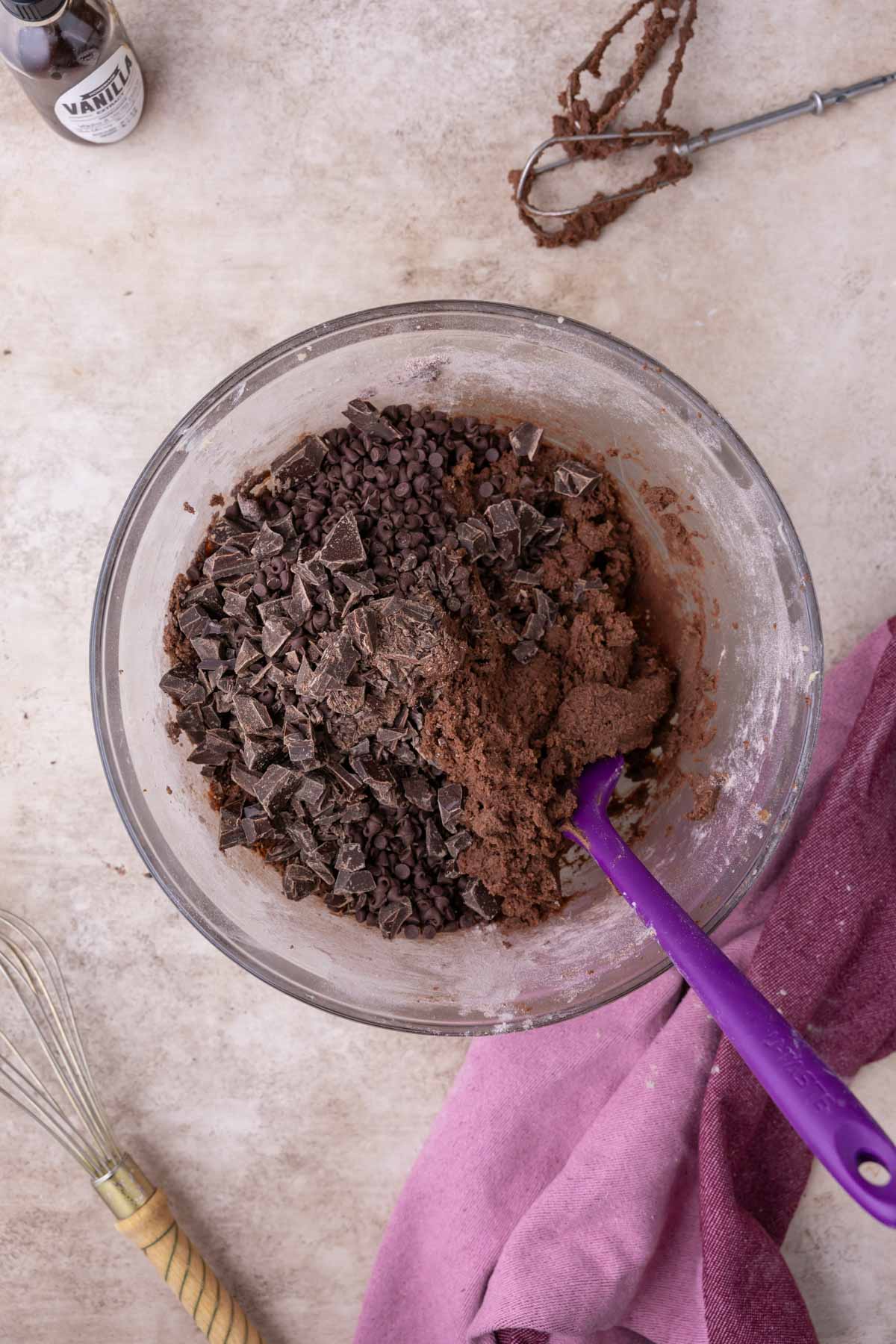 Chocolate chunks being folded into a thick chocolate cookie dough.