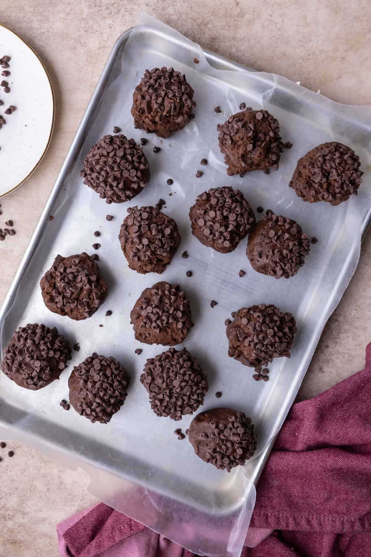 Overhead view of huge double chocolate cookie dough balls on a baking sheet before freezing.