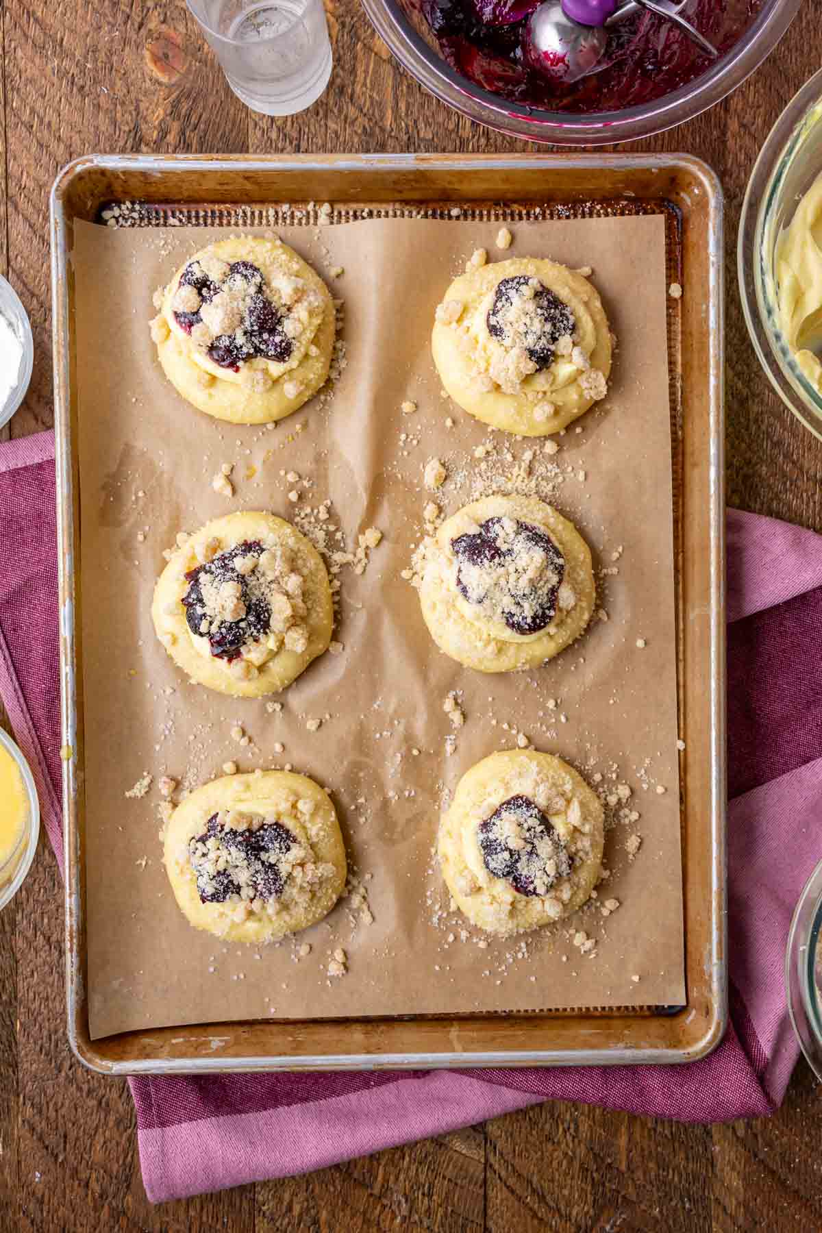 Overhead view of unbaked buns filled with cream cheese, blueberries, and streusel.