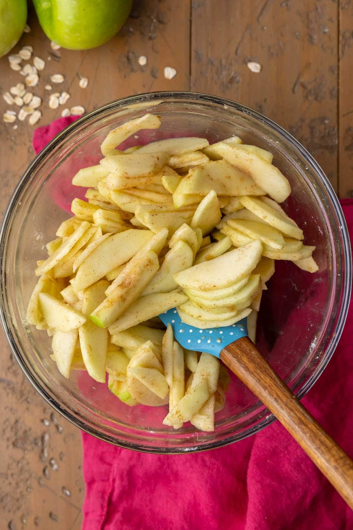 Stirring together sliced apples, flour, sugar, and spices in a glass bowl.