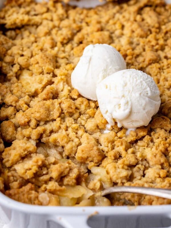 Close-up view of apple crumble in a baking dish with two scoops of vanilla ice cream on top.