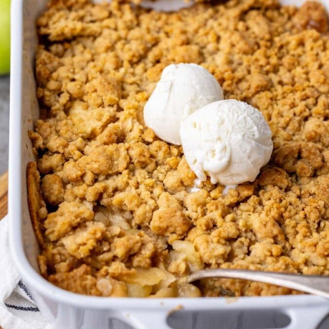Close-up view of apple crumble in a baking dish with two scoops of vanilla ice cream on top.