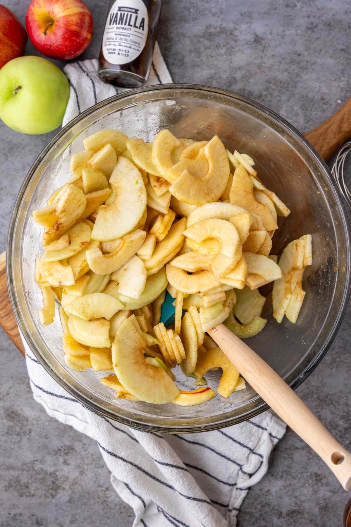 Overhead view of a bowl of sliced apples being tossed with cinnamon and sugar.