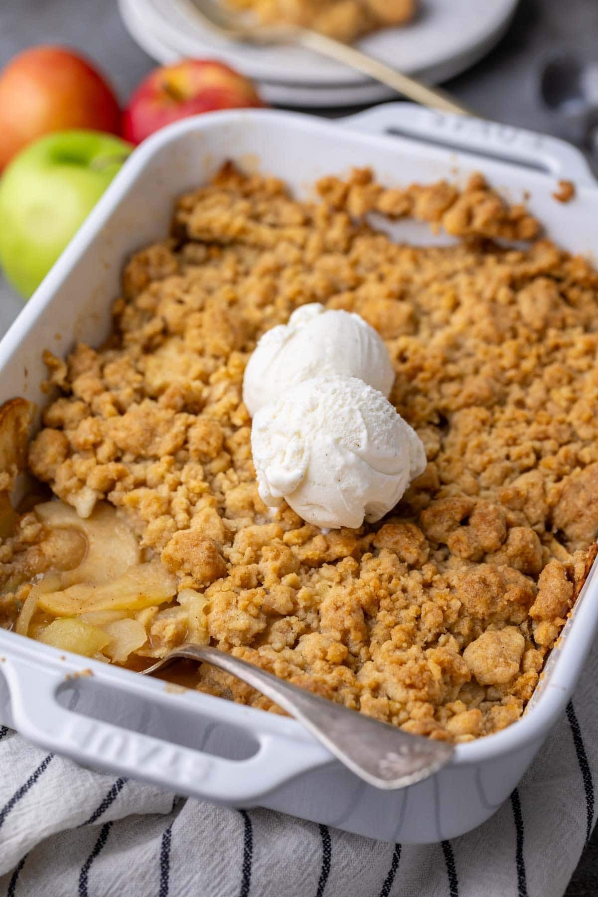 Close-up view of an apple dessert with a golden brown, crisp crumble topping and scoops of vanilla ice cream on top.