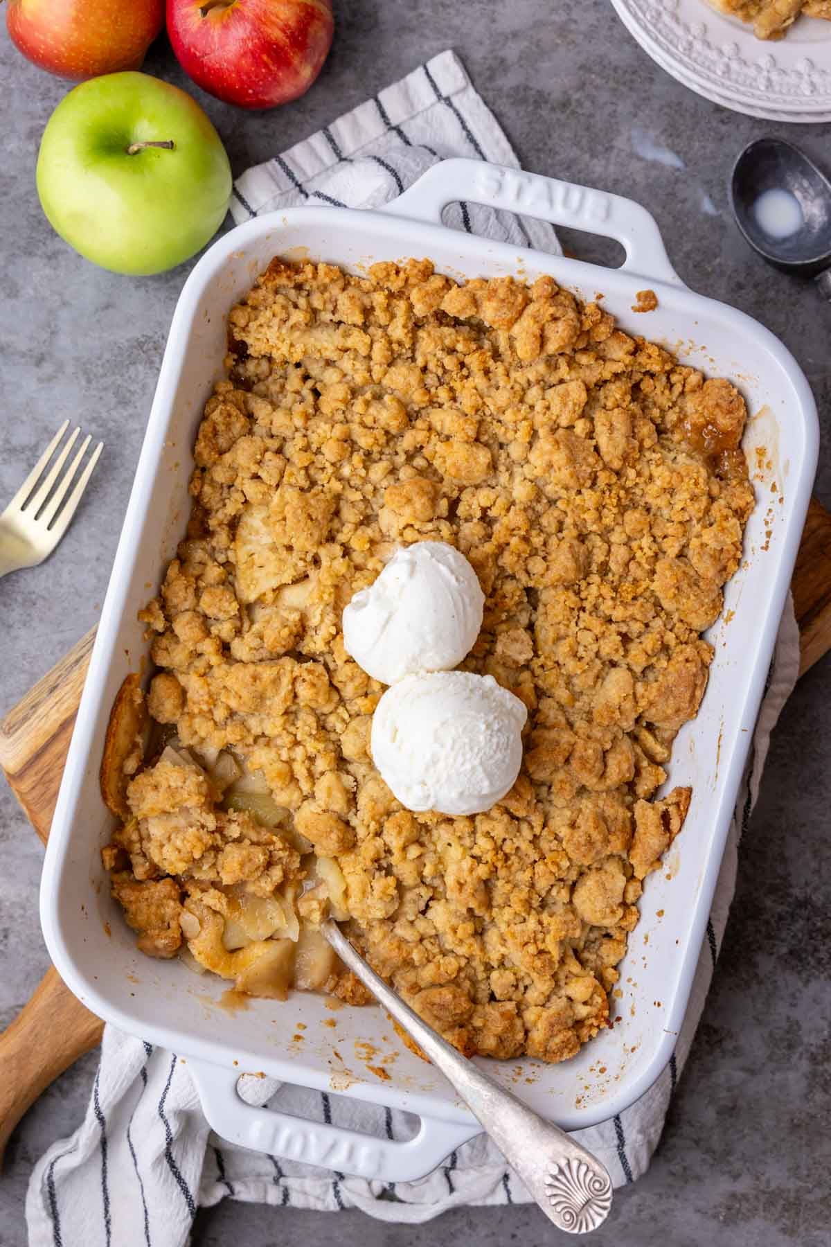 Overhead view of apple crumble in a baking dish with two scoops of vanilla ice cream on top.