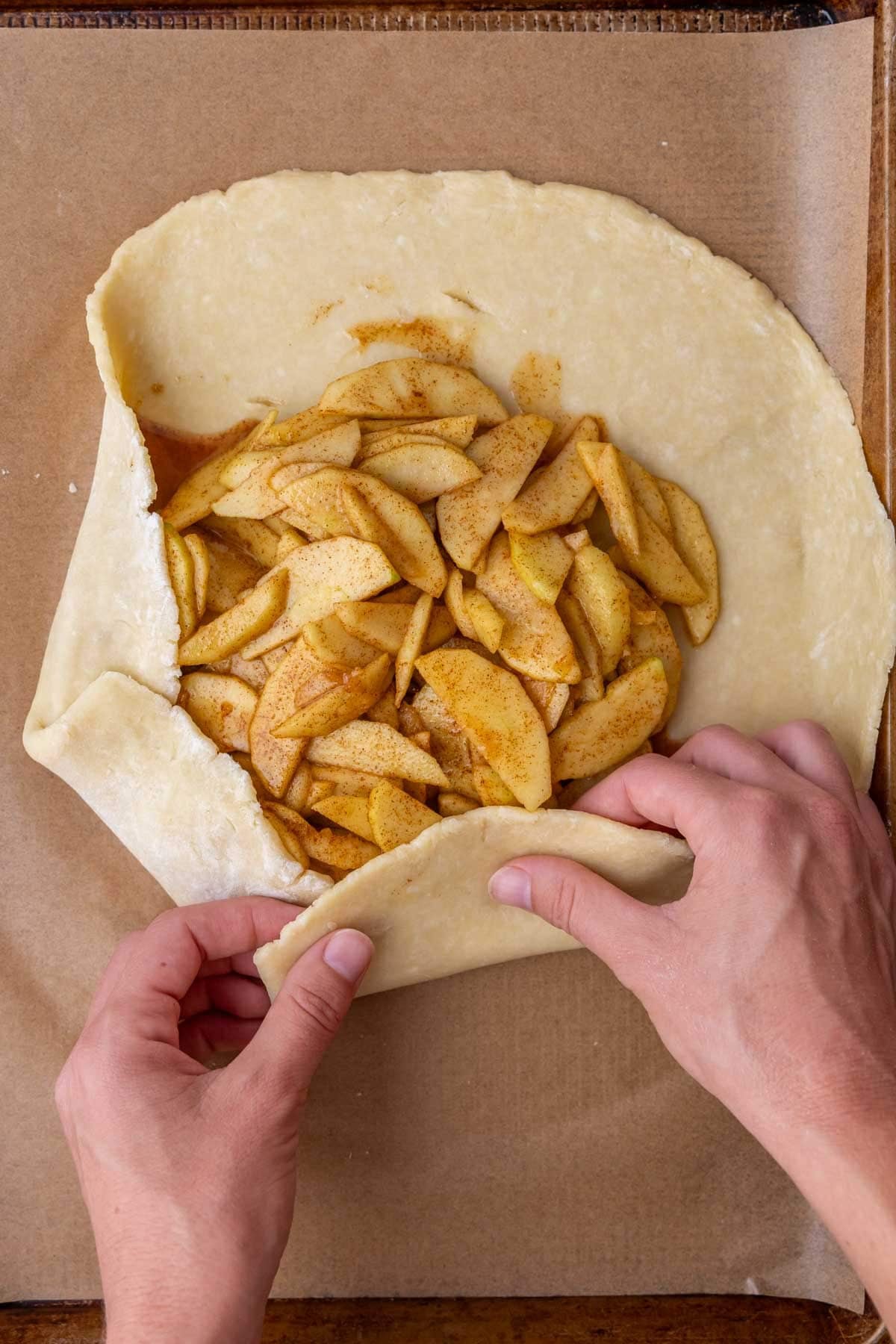 Hands folding pie crust rustically over an apple filling.