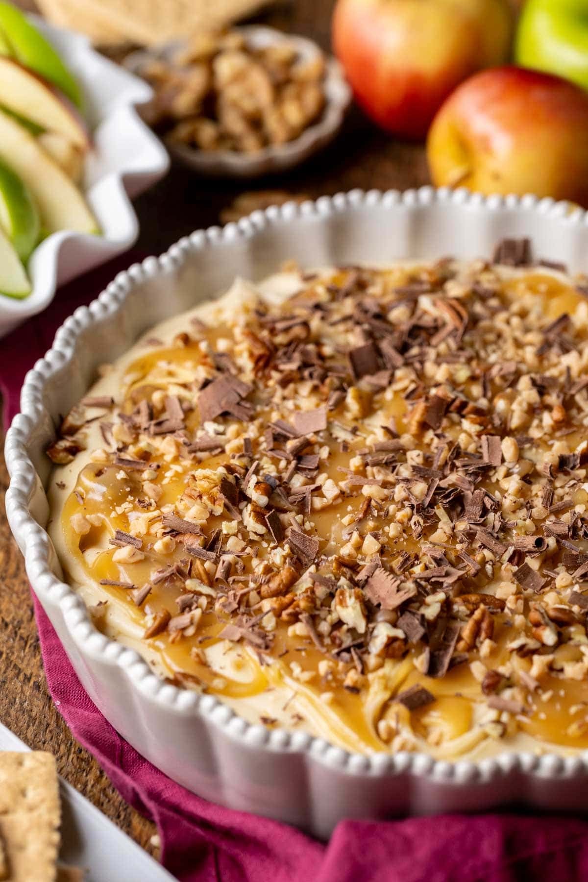 Close-up view of a cheesecake dip for apples topped with caramel, pecans, and shaved chocolate.