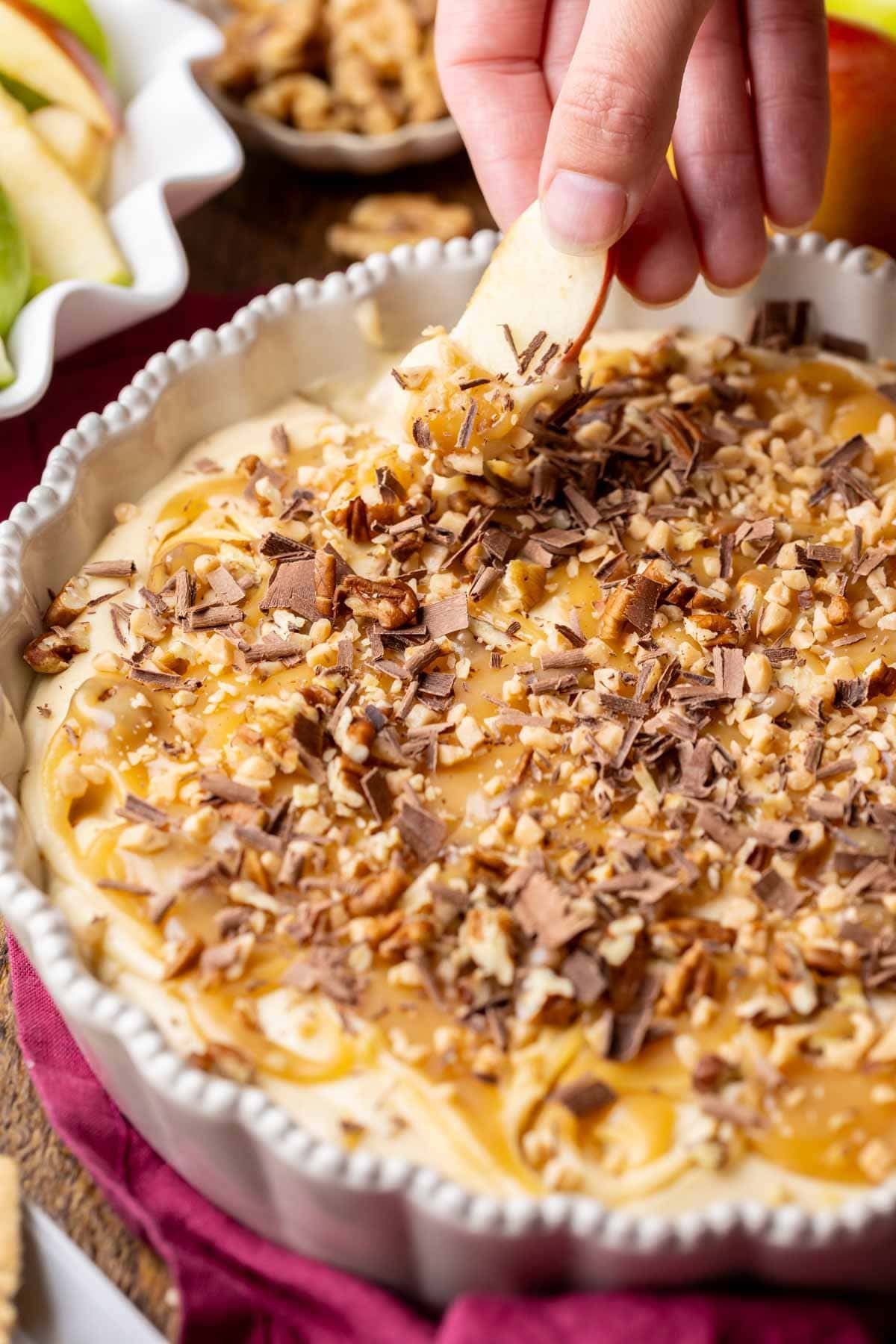 Apple slice being dipped into a caramel cheesecake dip.
