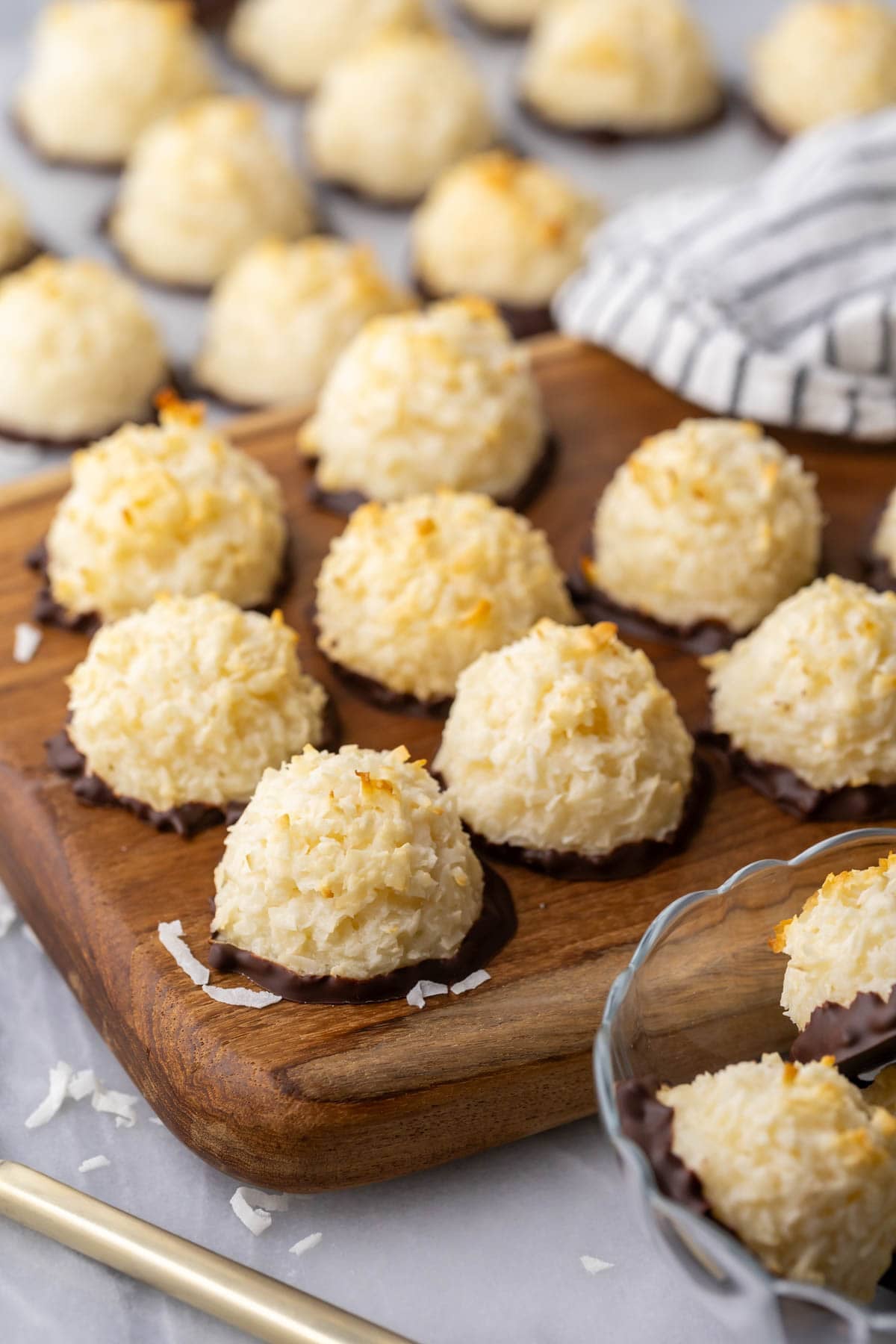 Coconut macaroons that have been dipped in chocolate resting on a wood cutting board.